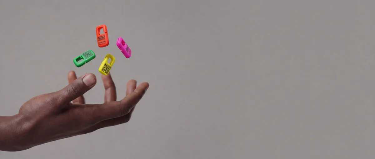Four Premium QR Tags, orange, green, yellow and pink, in the air above an open hand